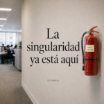 Pasillo de oficina con empleados trabajando al fondo. En primer plano, sobre una pared clara, aparece el título “La singularidad ya está aquí” junto a un extintor rojo envuelto en plástico con una nota que dice “usar mañana”.