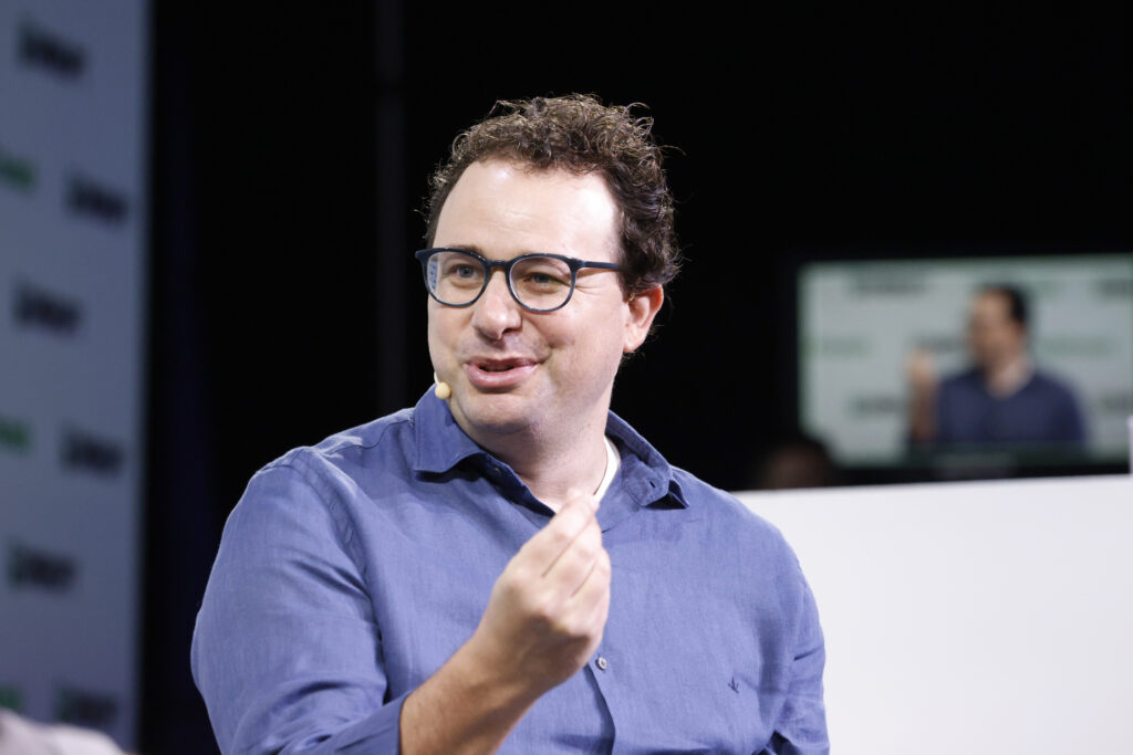 Dario Amodei, con gafas y camisa azul, gesticula durante TechCrunch Disrupt 2023.