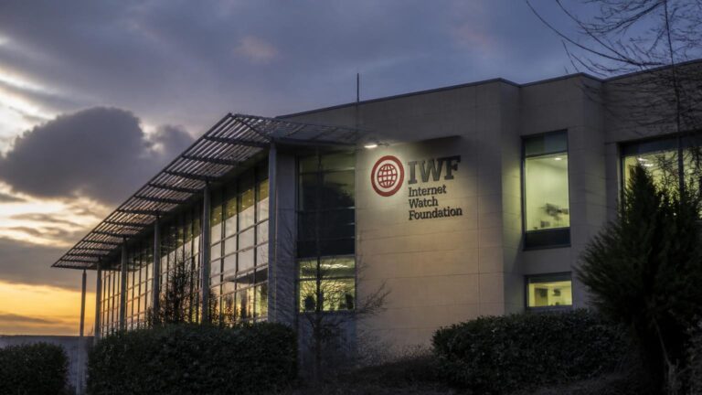 Exterior de un edificio con grandes ventanales, arbustos en primer plano y un rótulo que dice 'IWF Internet Watch Foundation'.